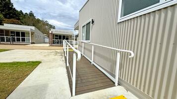 A building with a ramp leading to a door, a yellow tactile paving at the bottom, and a white railing along the ramp.
