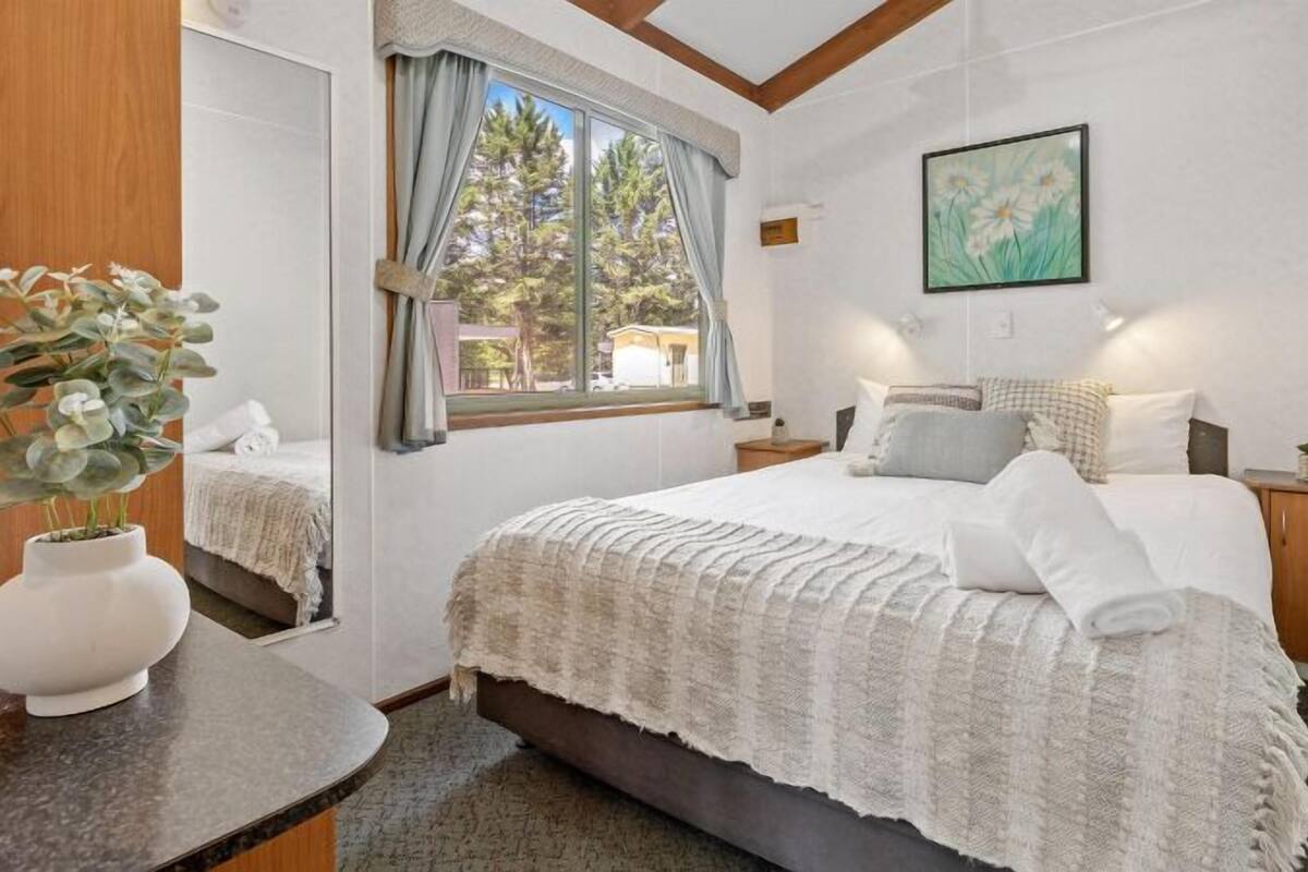 Quarto com uma cama grande, uma mesa de cabeceira com um vaso, uma janela com cortinas e um quadro na parede.