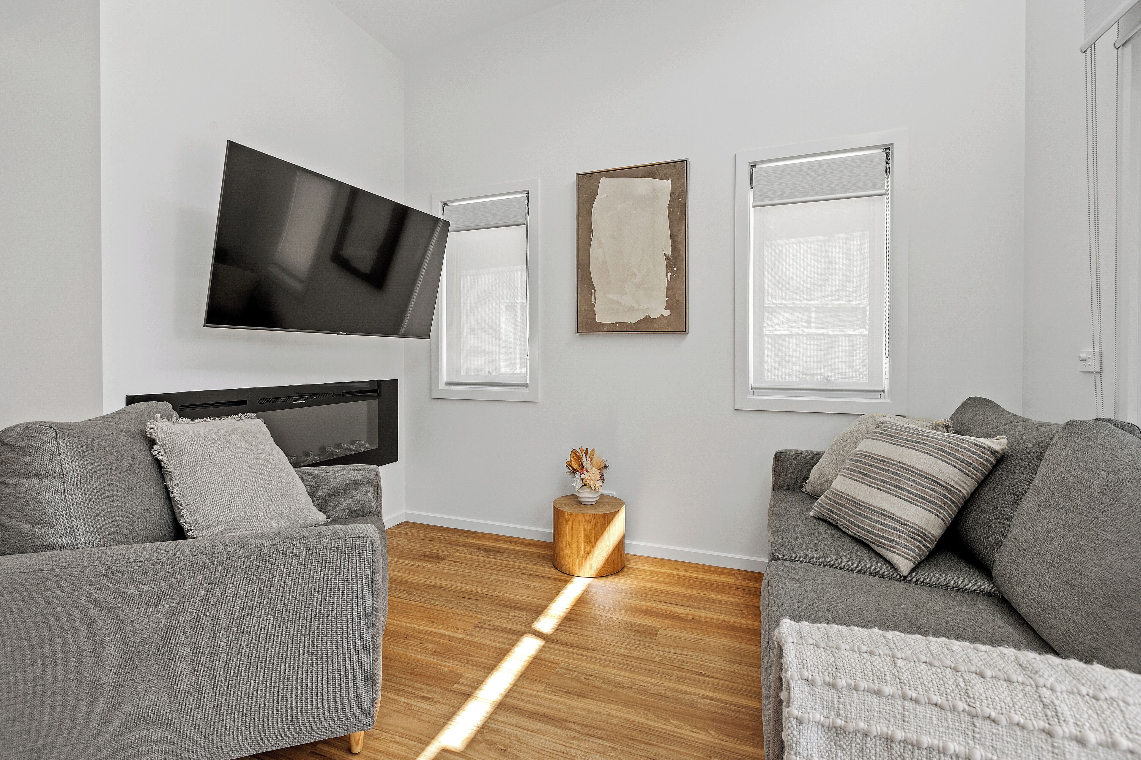 A modern living room with two grey sofas, a flat-screen TV, a round wooden coffee table, and a framed abstract painting.