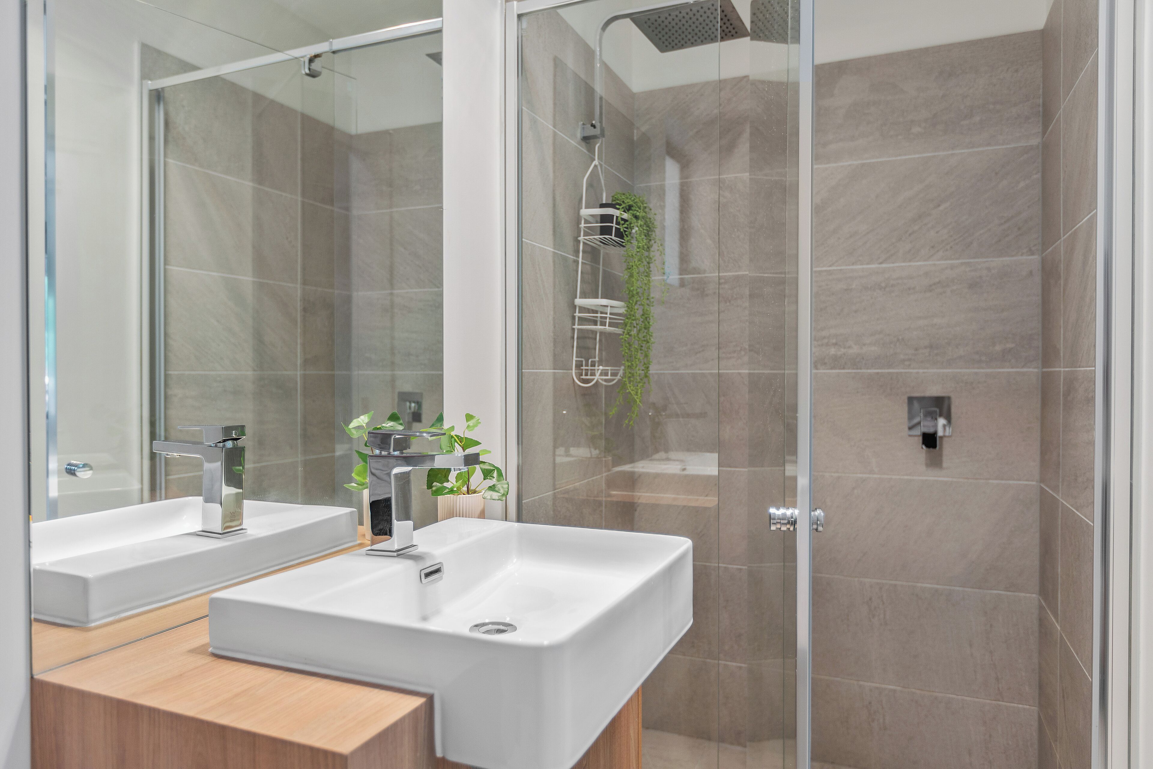 Une salle de bain moderne avec deux lavabos, une douche et un espace de douche séparé par des parois en verre.