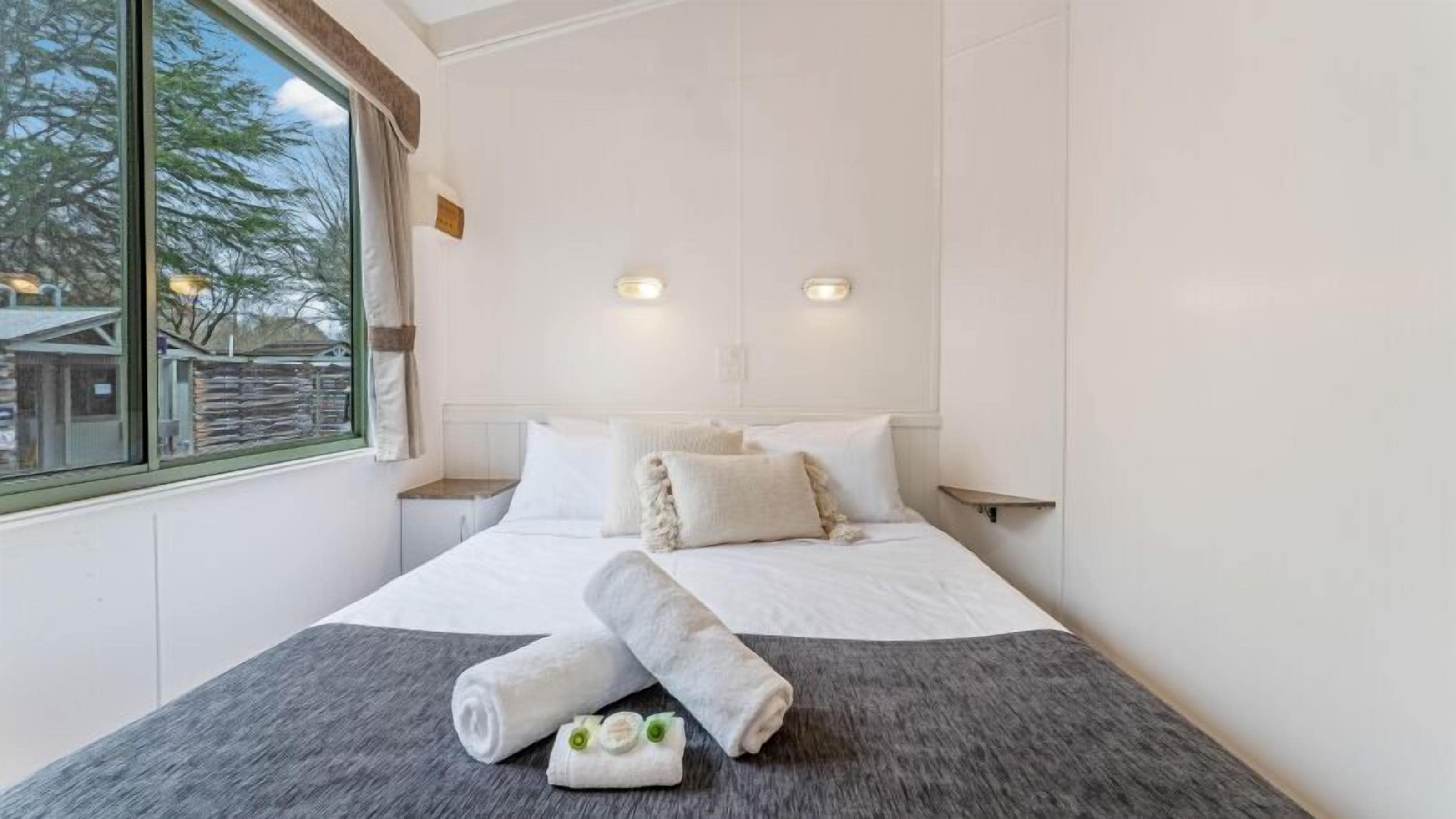 Une chambre d’hôtel avec un grand lit, deux tables de chevet, une fenêtre avec des rideaux et des lampes fixées au mur.