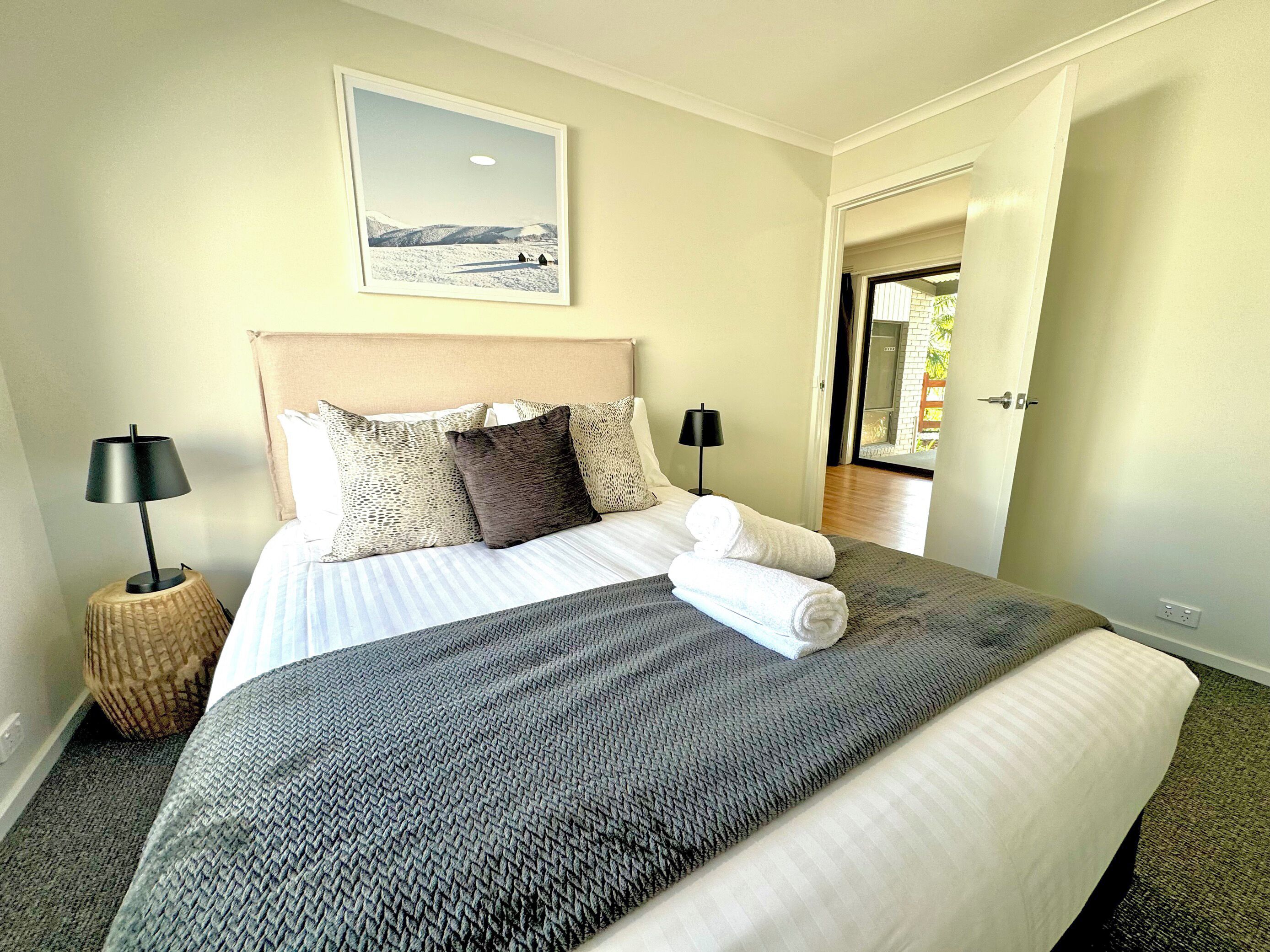 A neatly made bed with a headboard, two bedside lamps, and a framed picture on the wall.