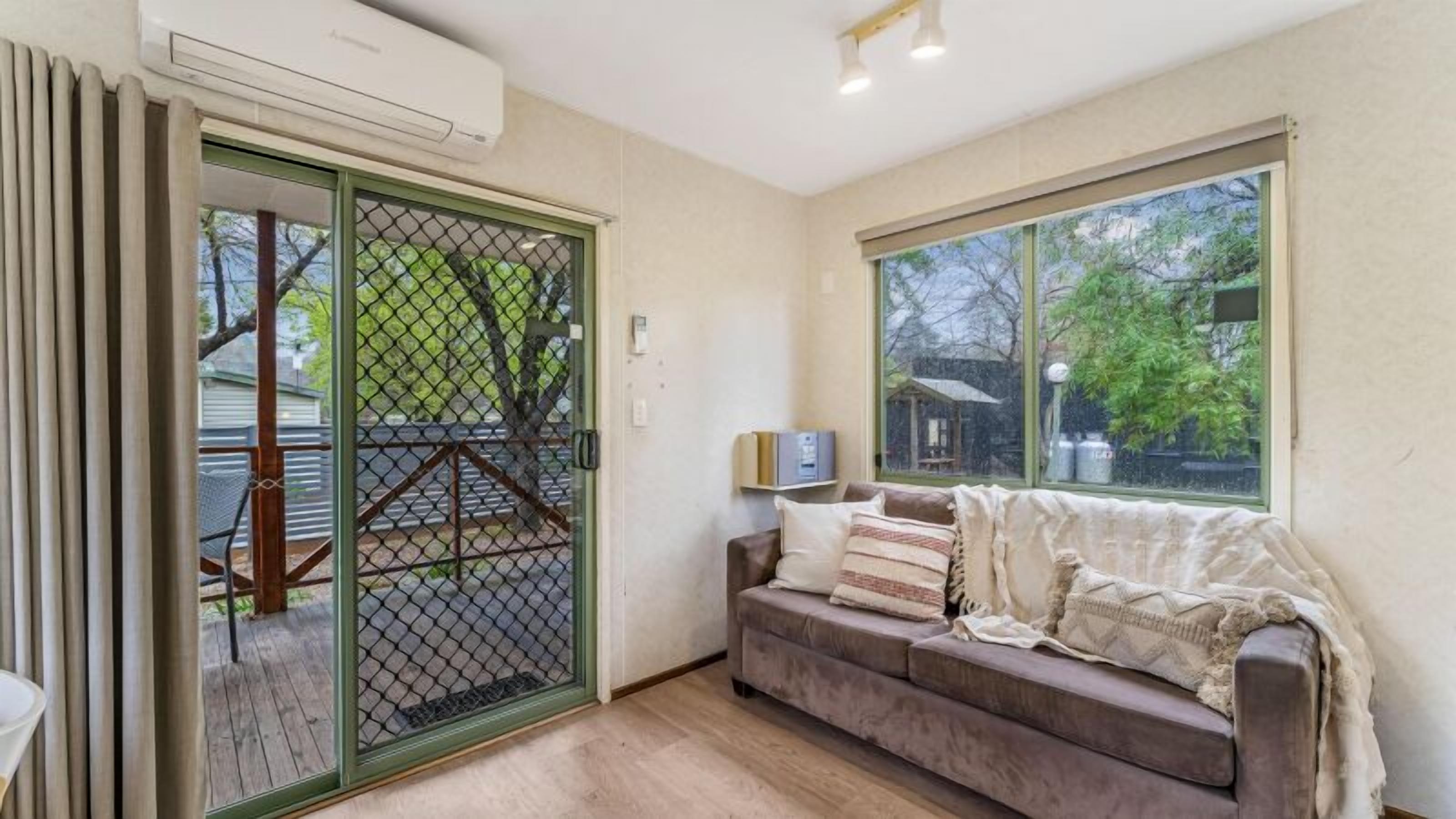 A room with a sliding glass door leading to an outdoor area, a cushioned sofa with multiple pillows, and a small table with a lamp.