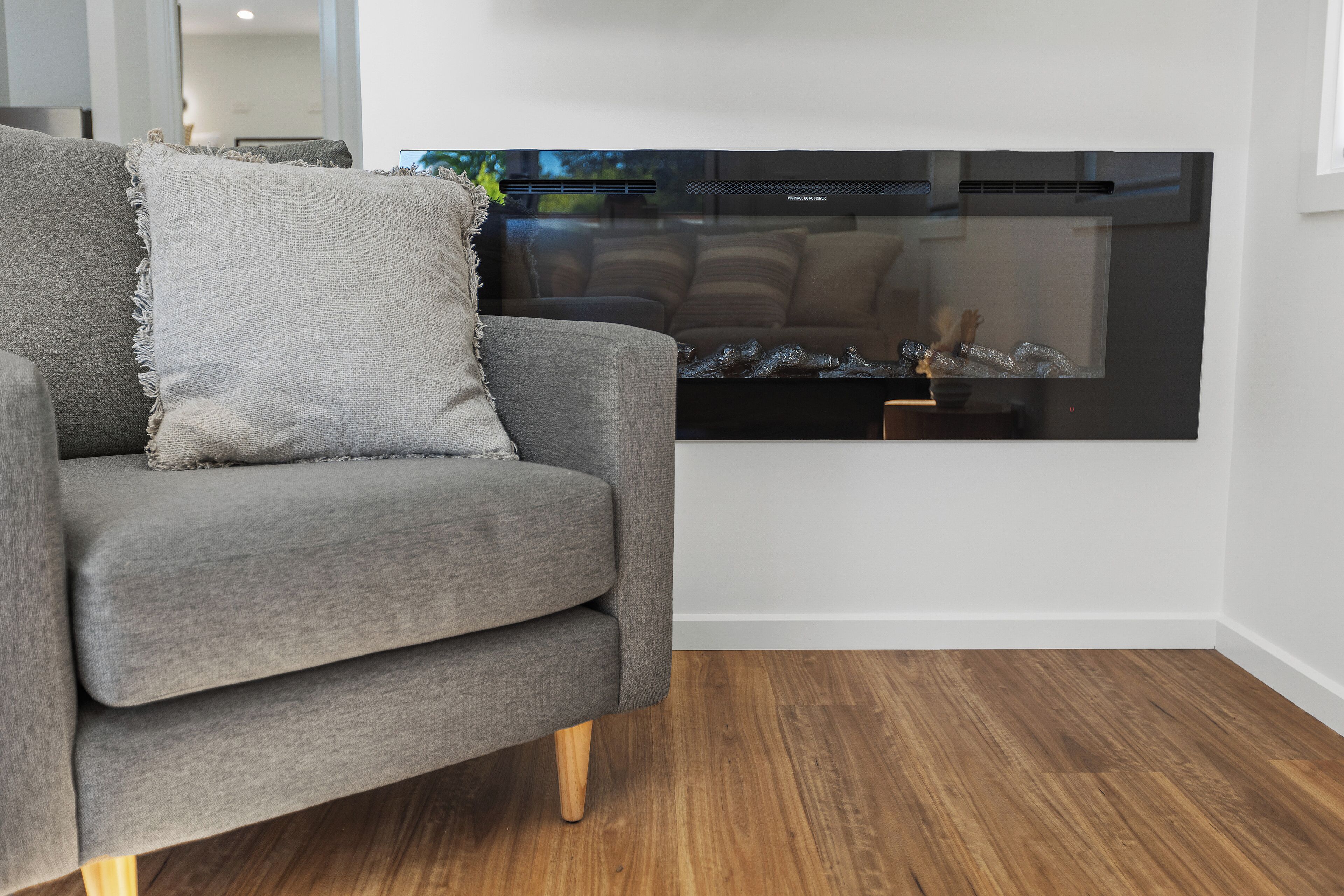 A modern living room with a grey sofa, a black fireplace, and wooden flooring.