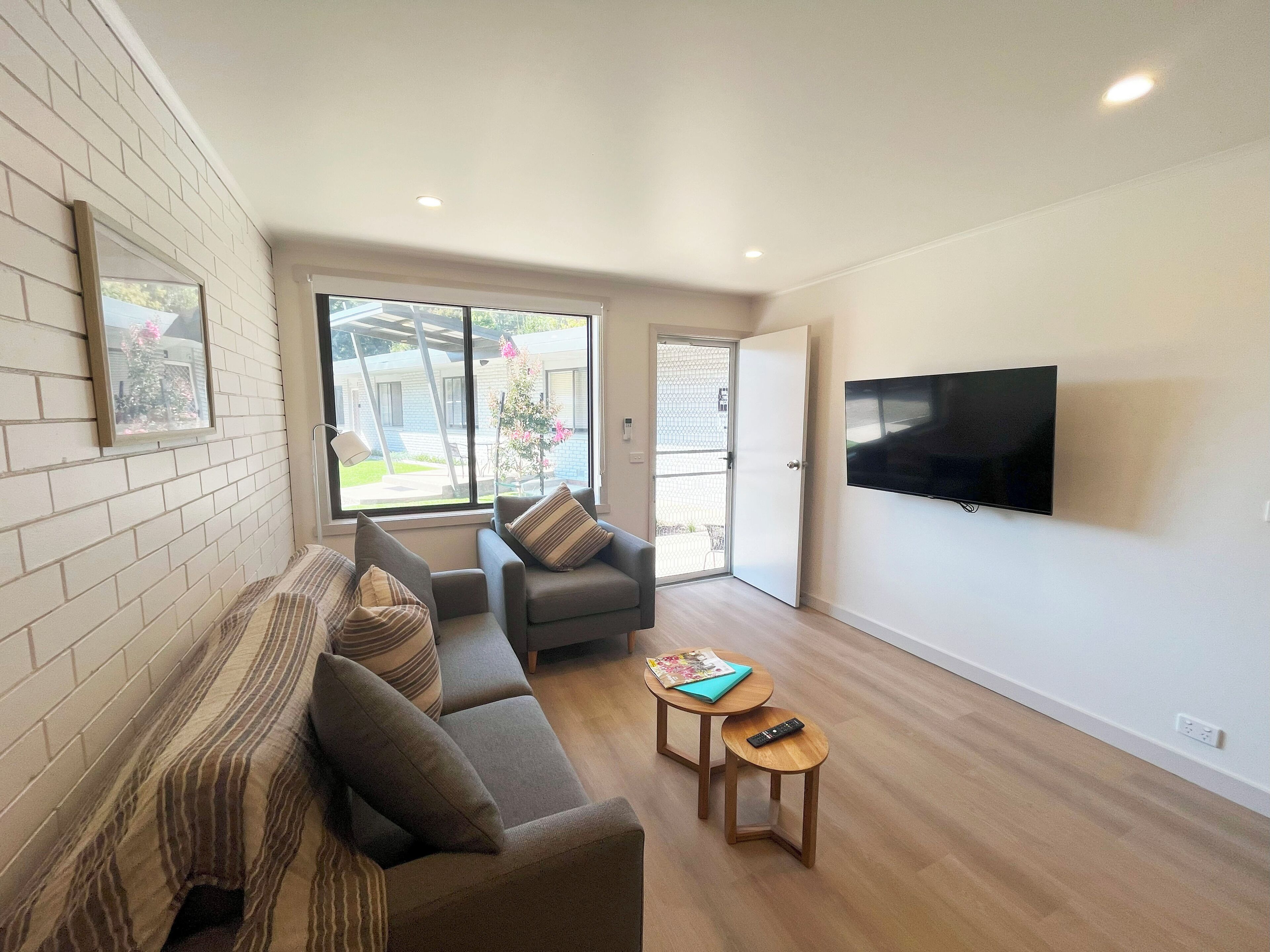 A modern living room with a sofa, armchair, and a TV mounted on the wall.
