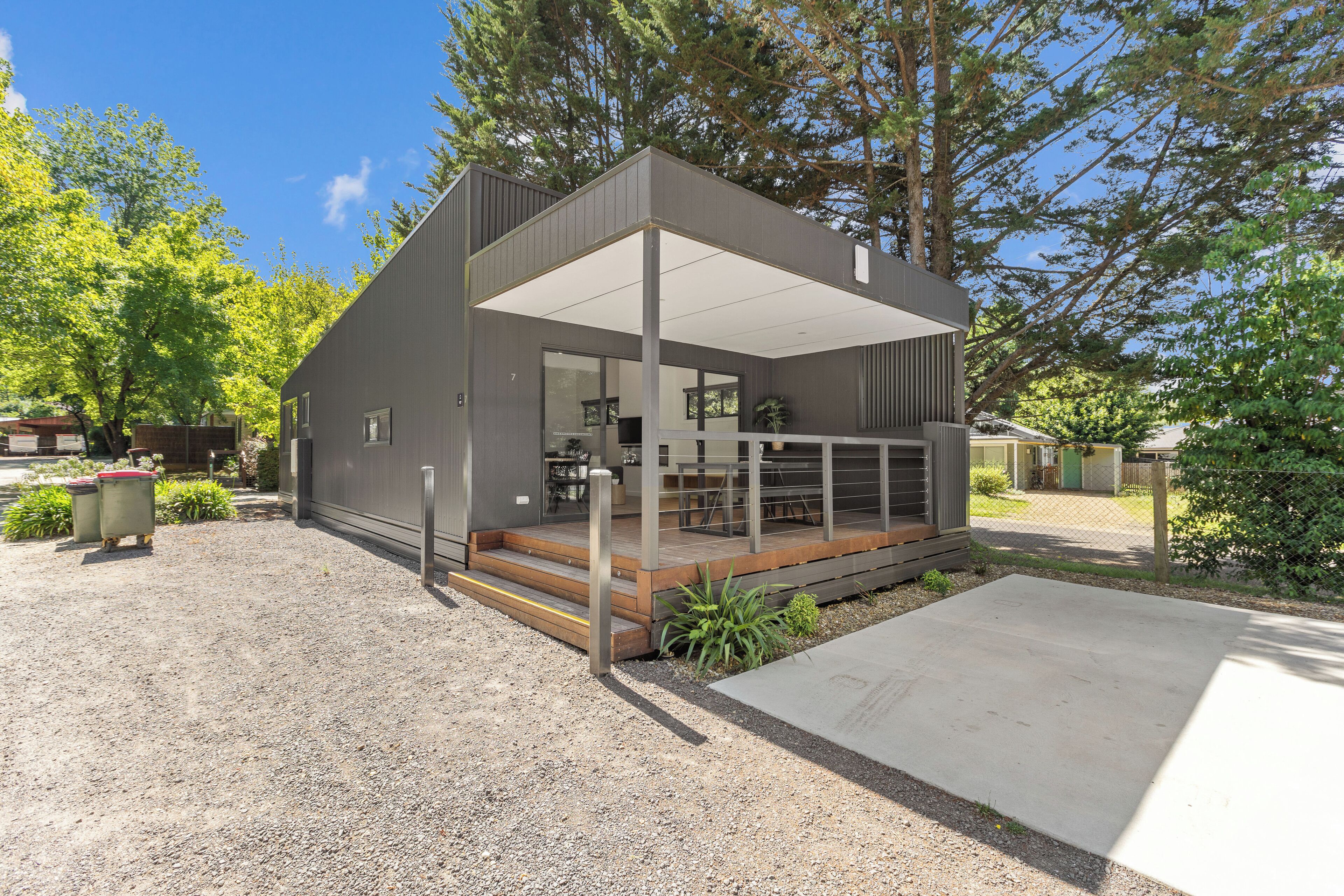 A modern house with a covered porch, a gravel driveway, and a wooden deck.