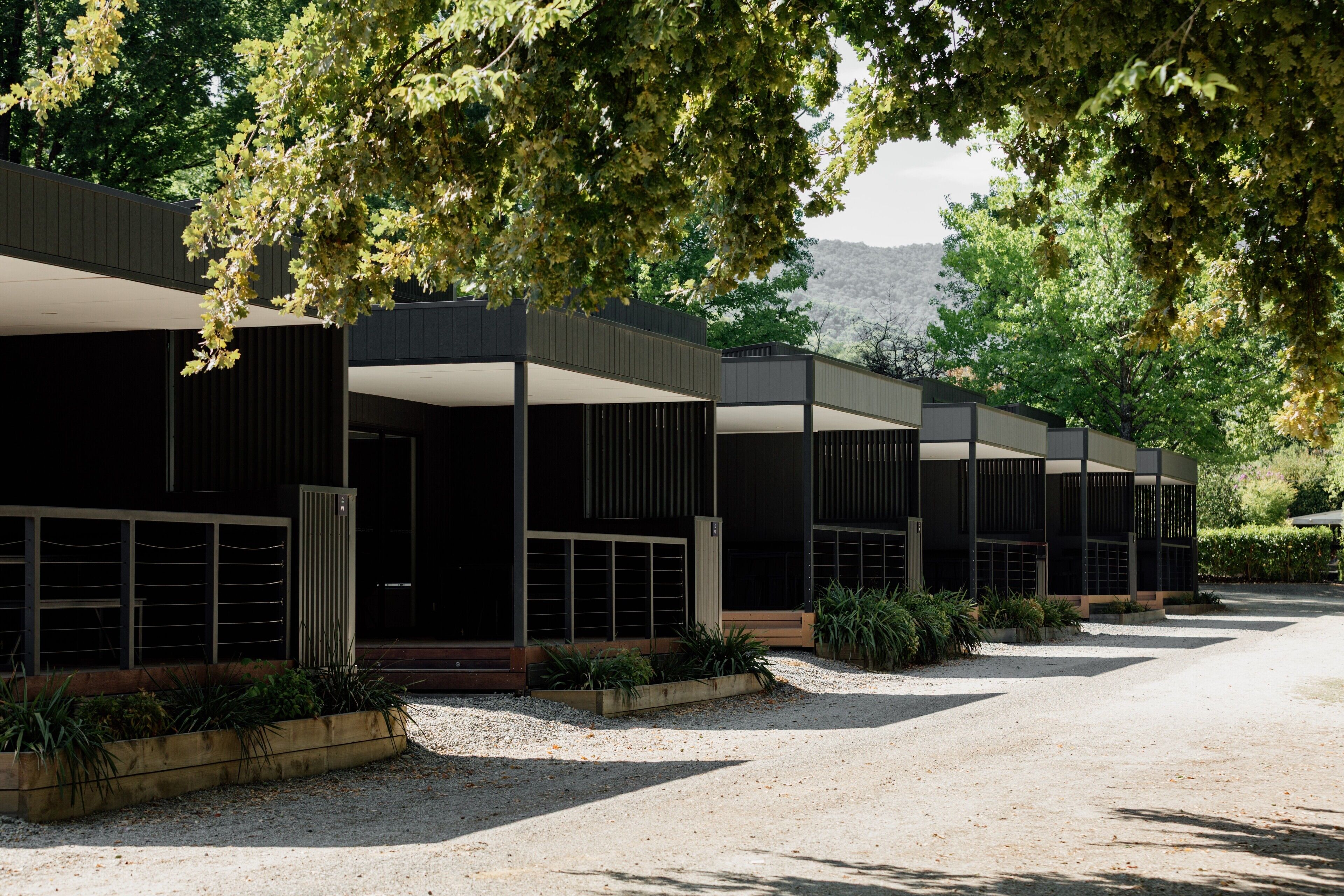 A modern building with multiple covered outdoor seating areas, surrounded by gravel and greenery.