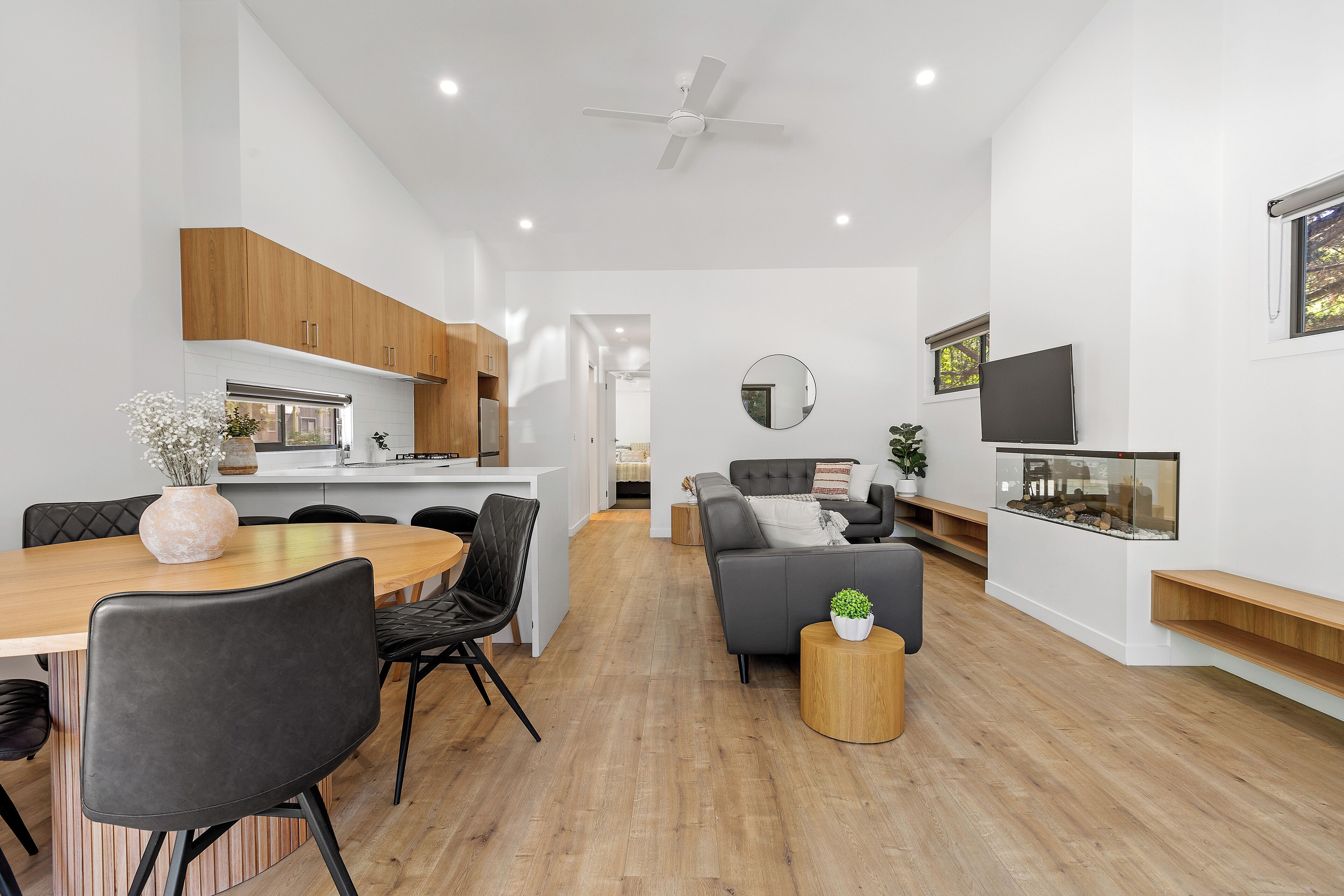 A modern living space with a dining area, a sofa, a TV, and a ceiling fan.