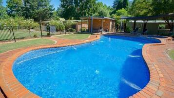 A swimming pool with a brick border, surrounded by a grassy area and trees.