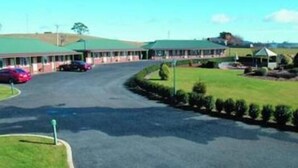 Un motel con techo verde, estacionamiento y un área verde con un pequeño edificio.