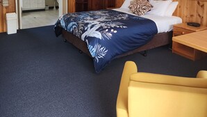 Una habitación de hotel con una cama, un armario de madera, una mesita de noche, una silla amarilla y un cuadro en la pared.