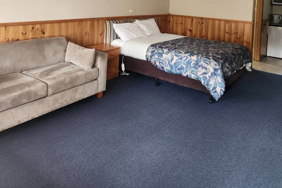 A room with a bed, a wooden headboard, a sofa, and a kitchenette area.