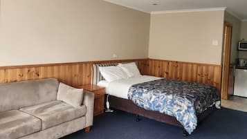 Una habitación con cama, cabecera de madera, sofá y zona de kitchenette.