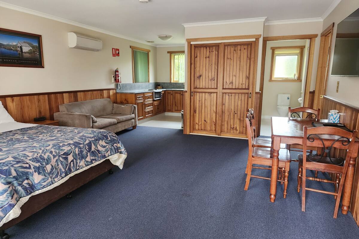 A bedroom with a bed, a sofa, a dining table with chairs, a kitchenette, and a bathroom.