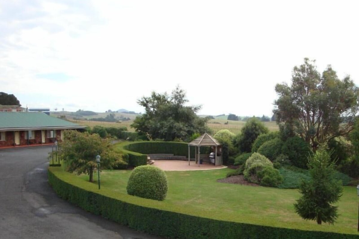 A building with a green roof, a paved driveway, and a well-maintained lawn with a gazebo.