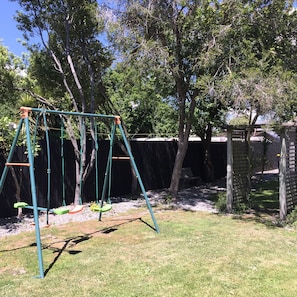 A swing set in a backyard with trees and a fence. - Ferry Motel (Christchurch)