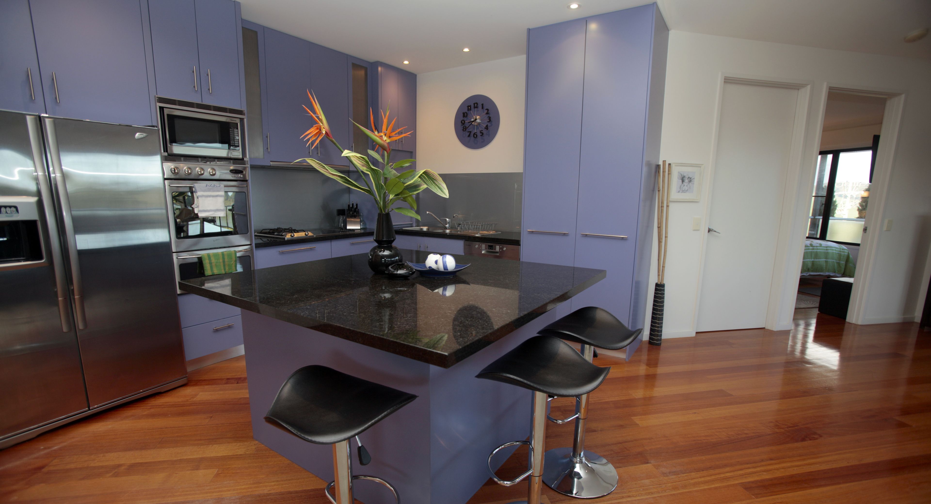A modern kitchen with a central island, bar stools, stainless steel appliances, and a decorative plant.