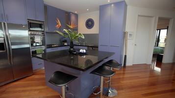 A modern kitchen with a central island, bar stools, stainless steel appliances, and a decorative plant.