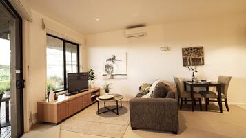 A modern living room with a television, sofa, dining table, and chairs.