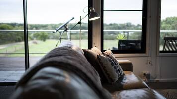 A room with a large window, a telescope, and a couch with pillows.