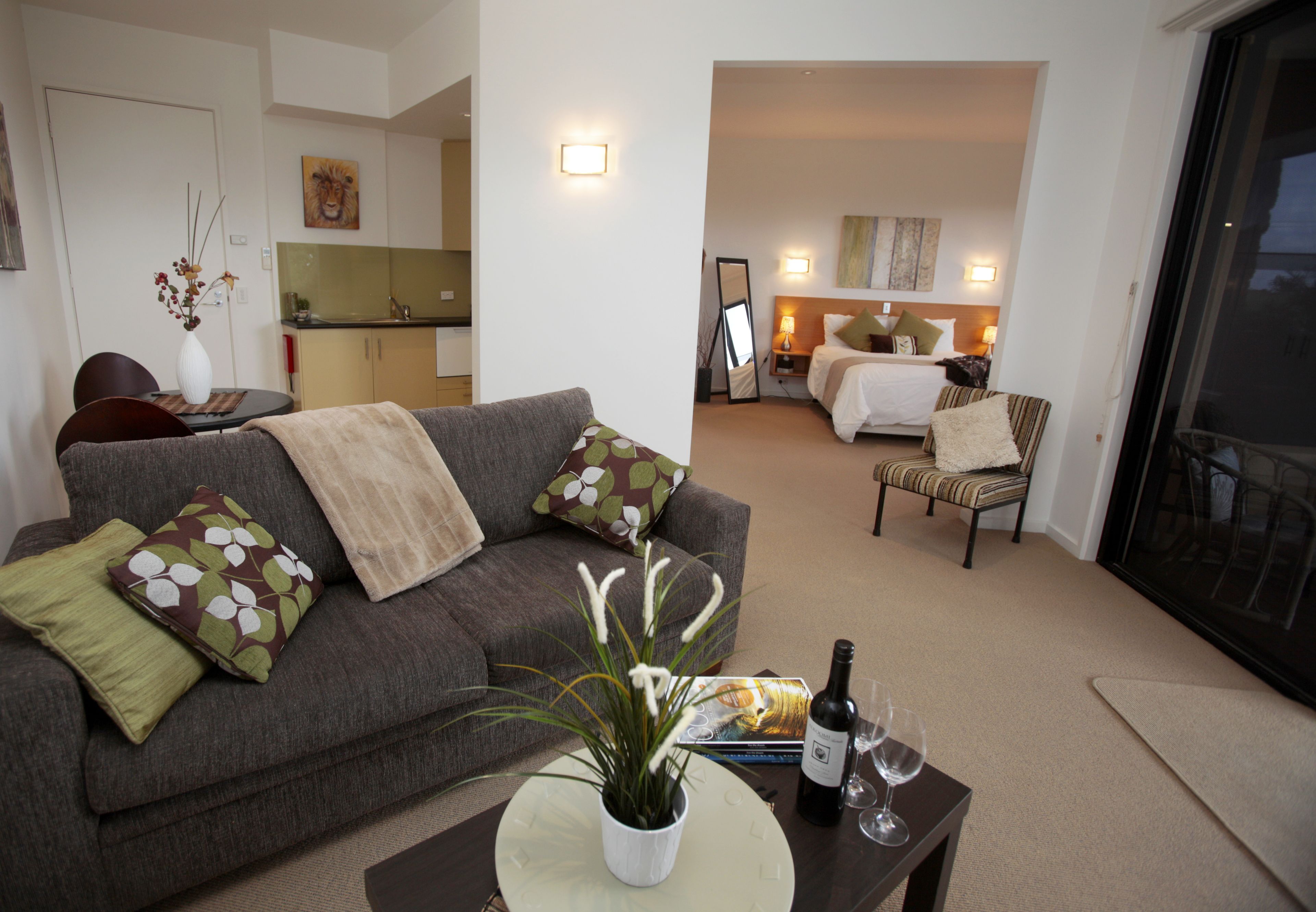 A living room with a sofa, a coffee table with a plant and wine glasses, and a dining area with a table and chairs.