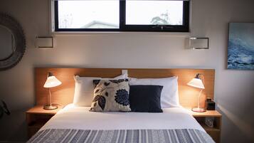 A neatly made bed with two bedside lamps, a window above, and a wall-mounted picture.