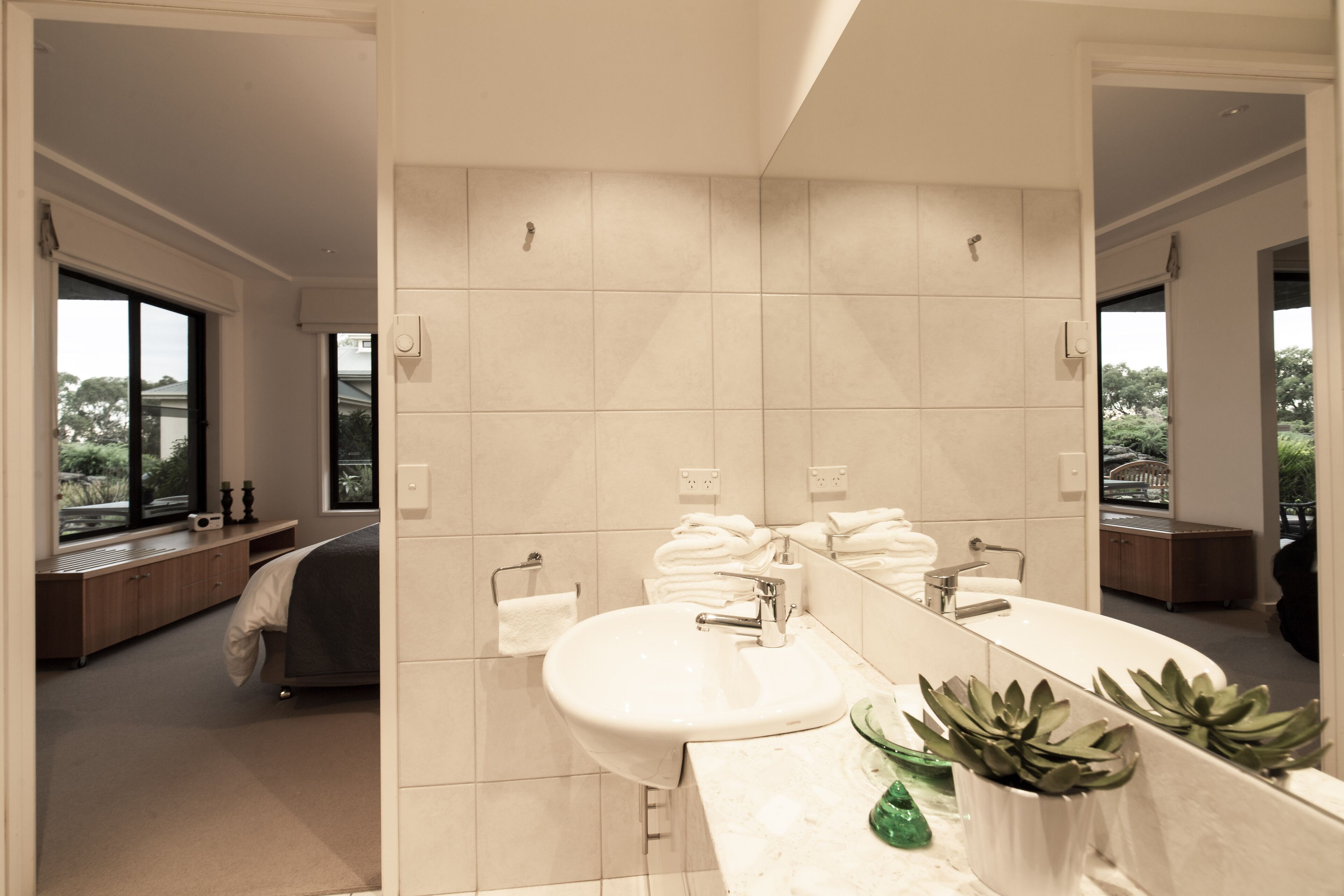 A modern bathroom with a large mirror, a sink, and a bathtub. There is a window providing natural light and a view of the outdoors.