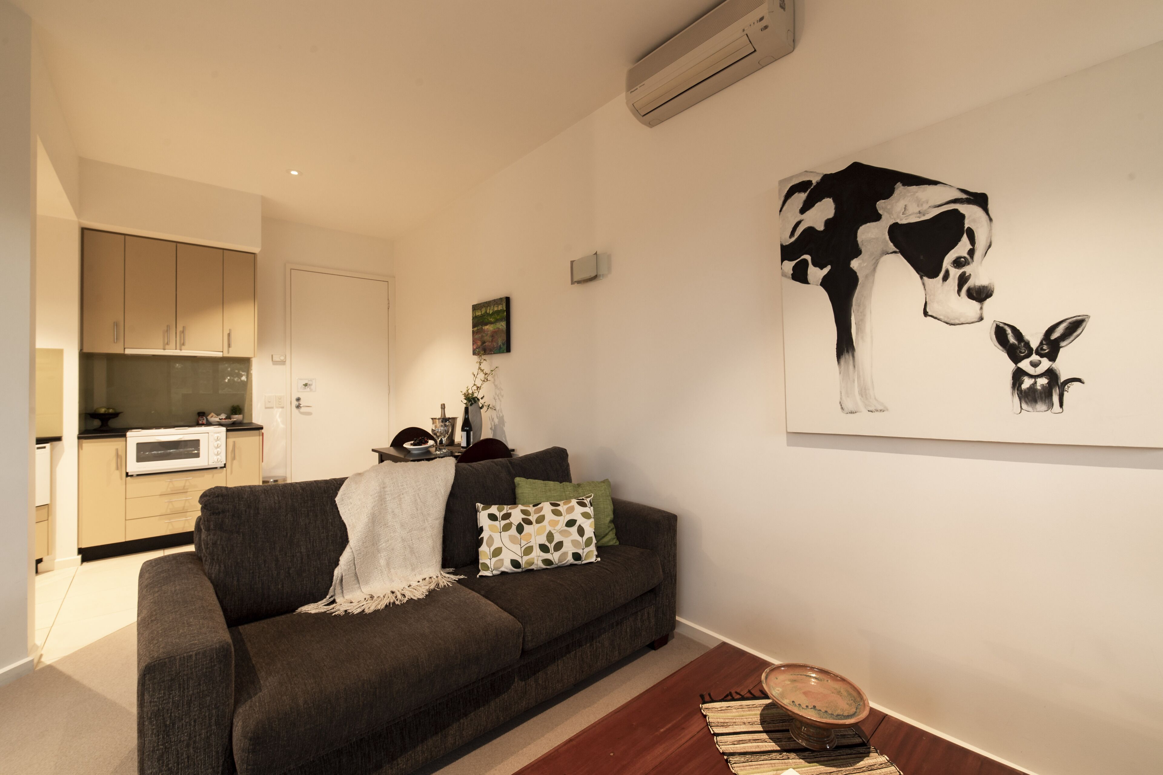 Un salón con un sofá gris oscuro, una mesita y una obra de arte colgada en la pared que representa una vaca y un conejo.