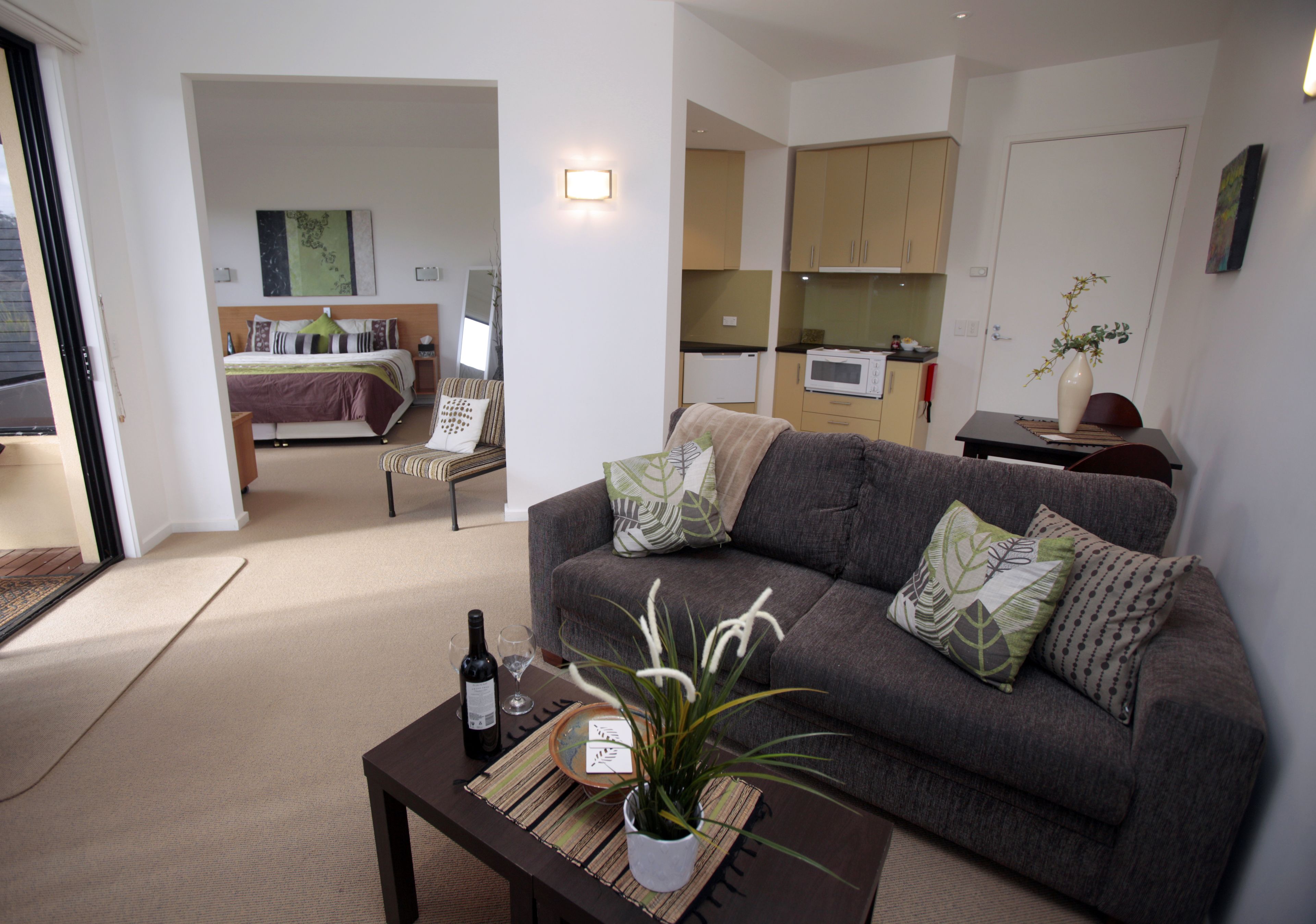A modern living room with a grey sofa, a coffee table with a plant, and a kitchen in the background.