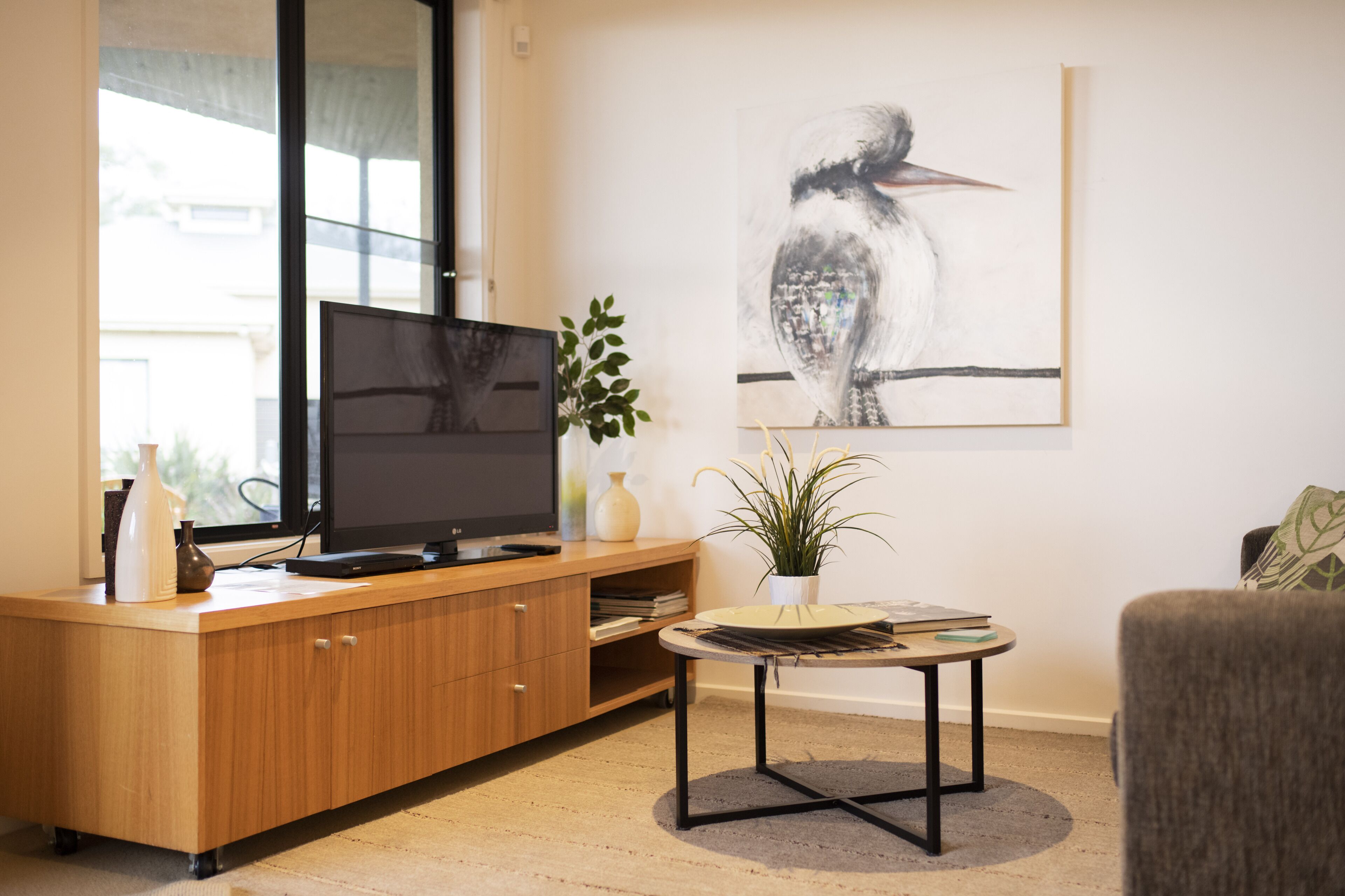 A modern living room with a wooden entertainment unit, a flat-screen TV, a round coffee table, and a large framed artwork on the wall.