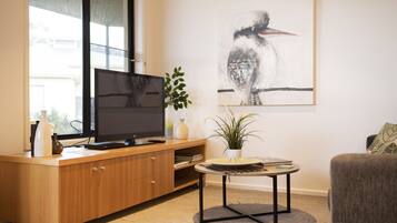 A modern living room with a wooden entertainment unit, a flat-screen TV, a round coffee table, and a large framed artwork on the wall.