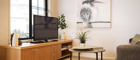 A modern living room with a wooden entertainment unit, a flat-screen TV, a round coffee table, and a large framed artwork on the wall.