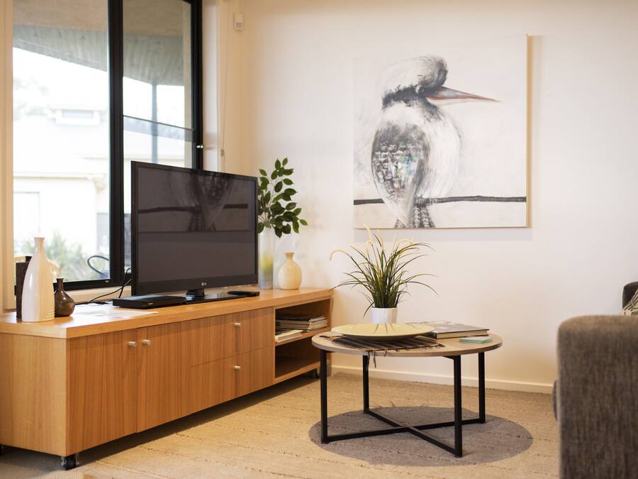 A modern living room with a wooden entertainment unit, a flat-screen TV, a round coffee table, and a large framed artwork on the wall.