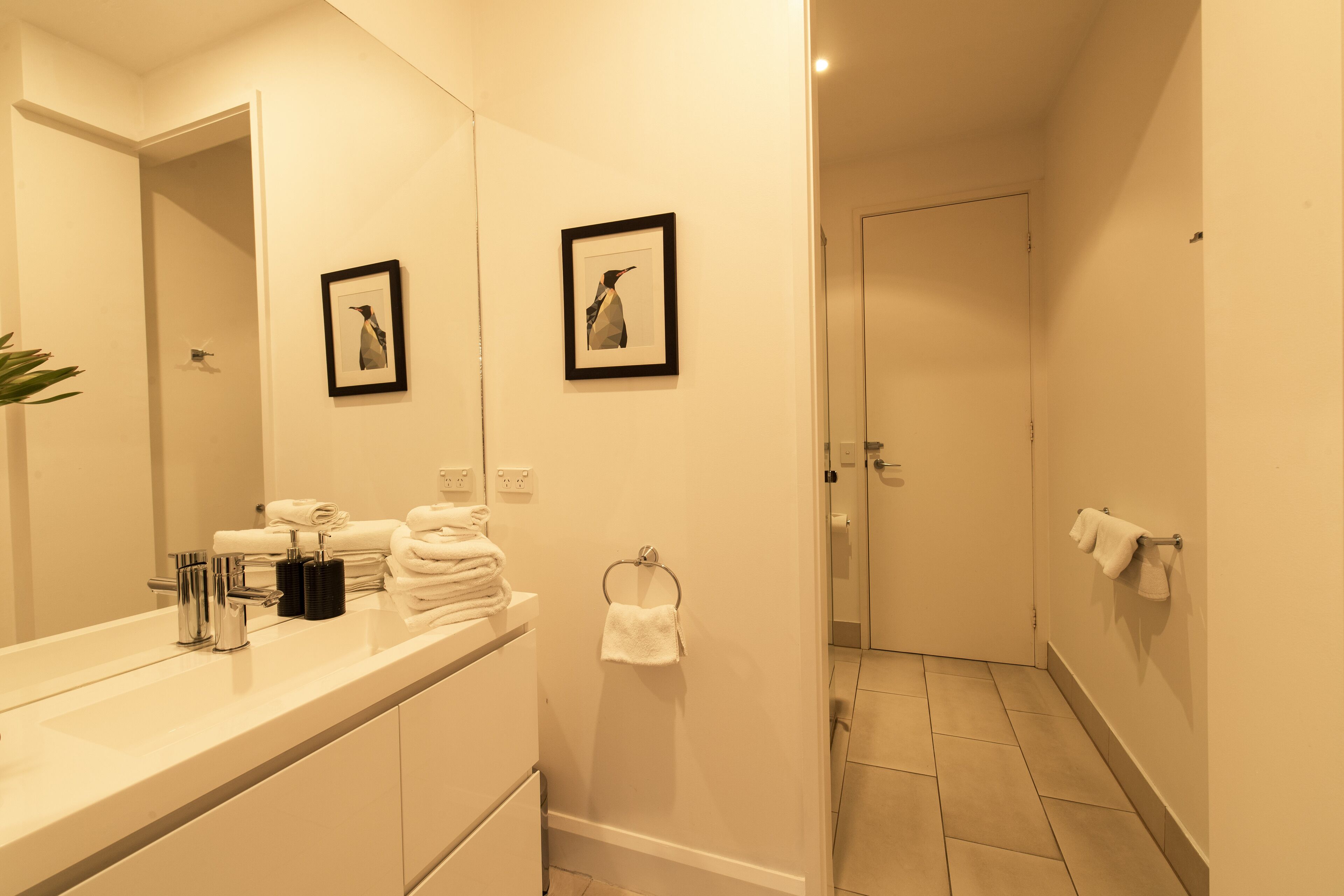 A modern bathroom with a large mirror, two framed pictures on the wall, a towel rack, and a sink with stacked towels.