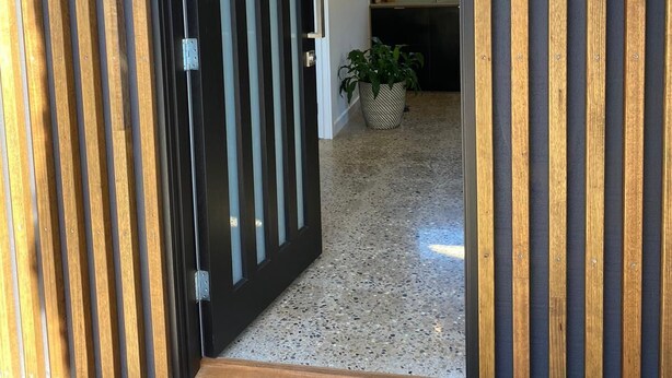Una entrada moderna con puerta de madera y suelo de hormigón.