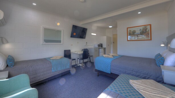 Ein Hotelzimmer mit zwei Einzelbetten, einem Schreibtisch mit Stuhl, einer Mikrowelle, einer kleinen Küchenzeile, einem an der Wand montierten Fernseher und einem Gemälde.