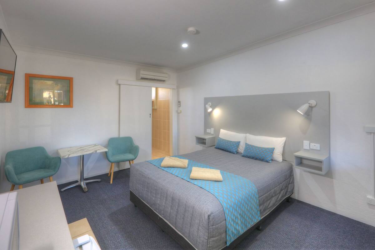A modern hotel room with a bed, two chairs, a small table, and a TV.