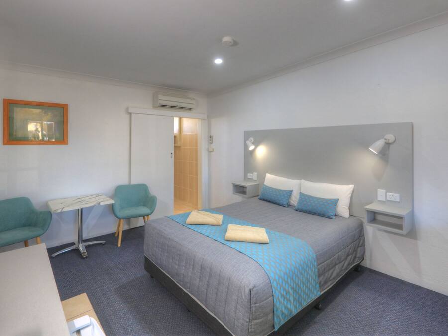 Ein modernes Hotelzimmer mit einem Bett, zwei Sesseln, einem kleinen Tisch und einem Fernseher.