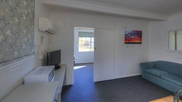 A room with a flat-screen TV, a white refrigerator, a blue sofa, and a painting on the wall.