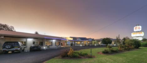 A motel with a signboard, a parking area, and a grassy lawn.