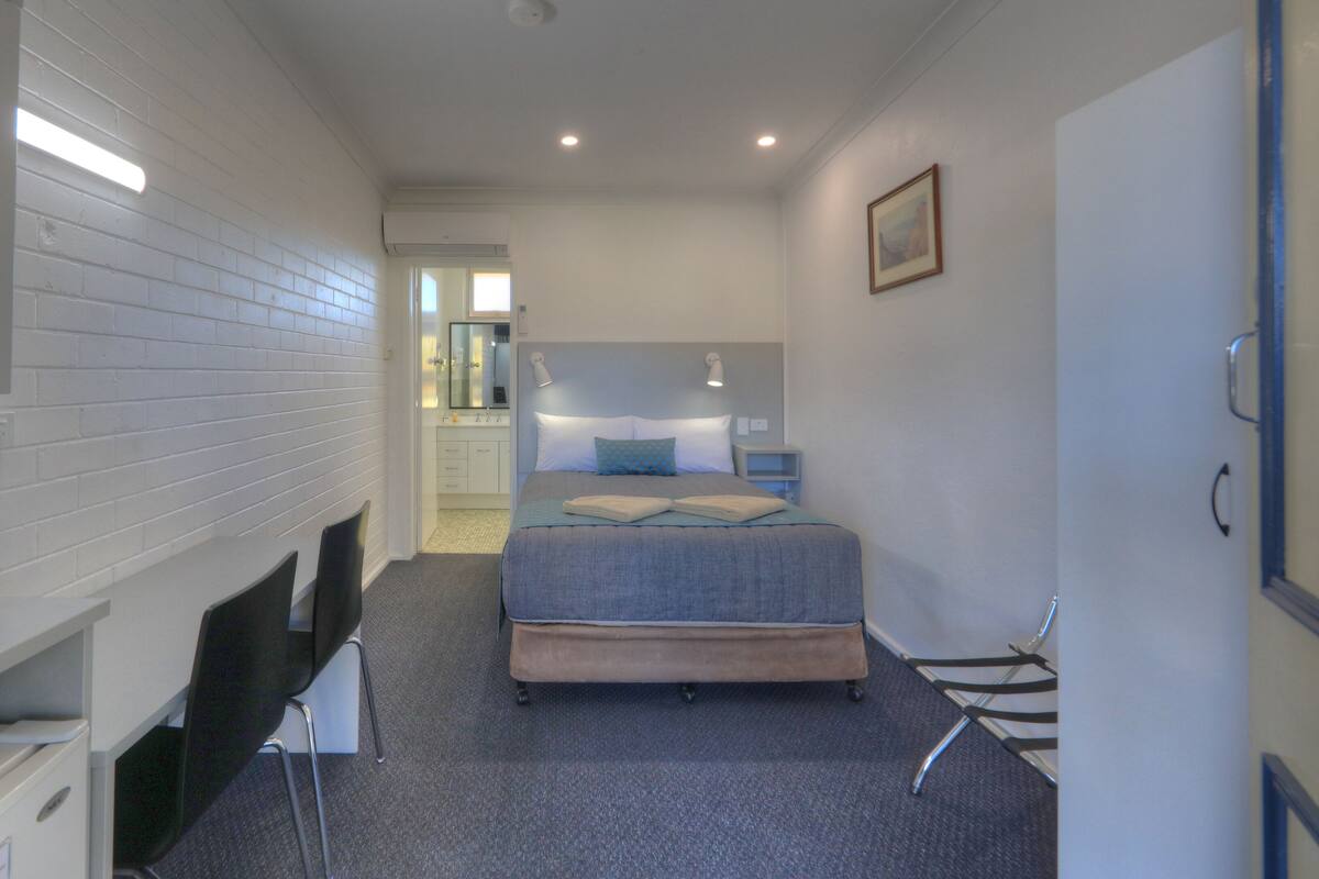 A bedroom with a bed, bedside tables, a desk with a chair, a microwave, and a wardrobe.