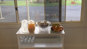 A breakfast table with a fruit bowl, a juice pitcher, and a plate of fruit. There are also several books and a gift box on the table. - Glen Innes Motel (Glen Innes)