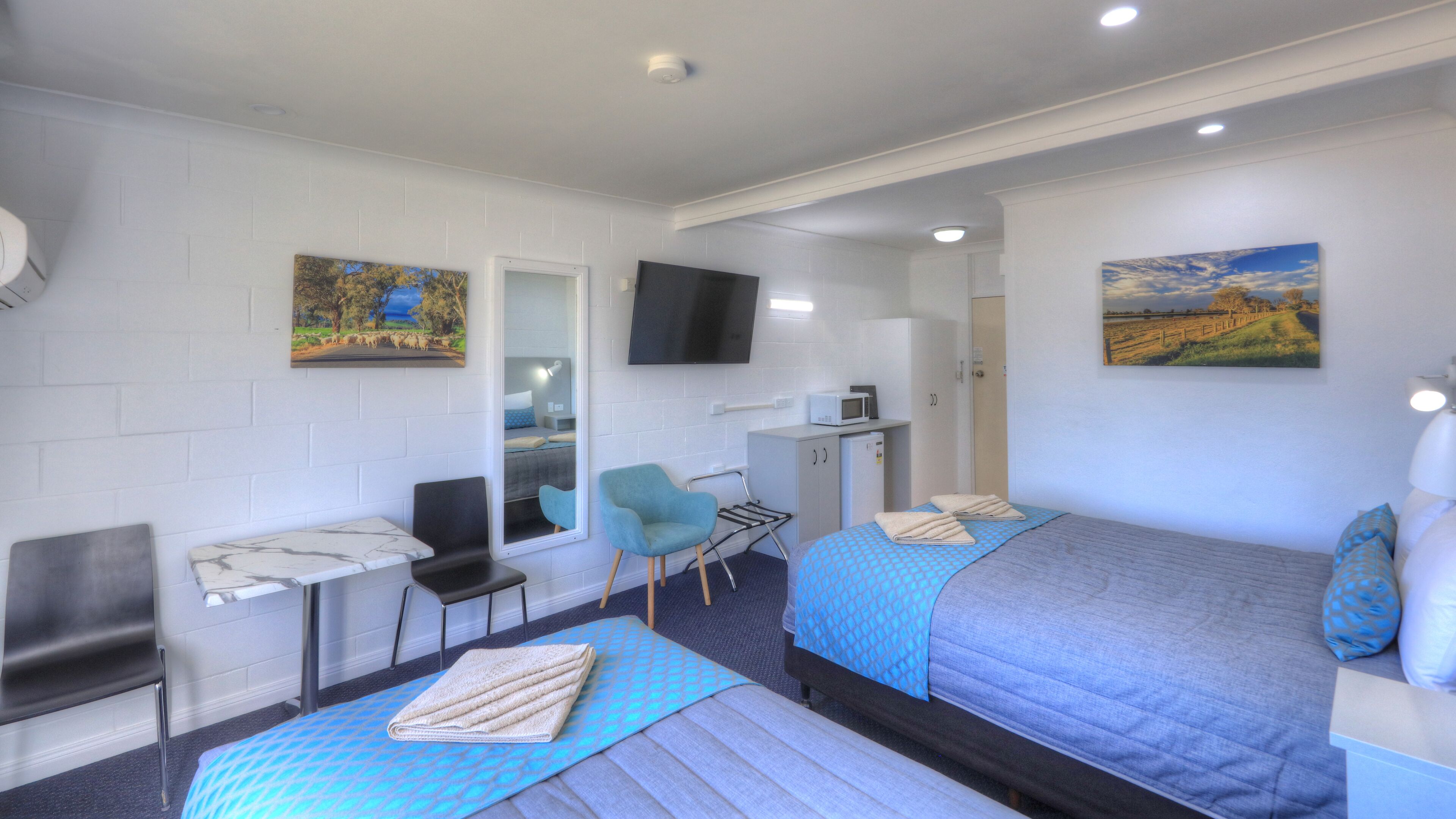 Habitación de hotel con dos camas, un escritorio, una silla, un televisor y obras de arte en las paredes.