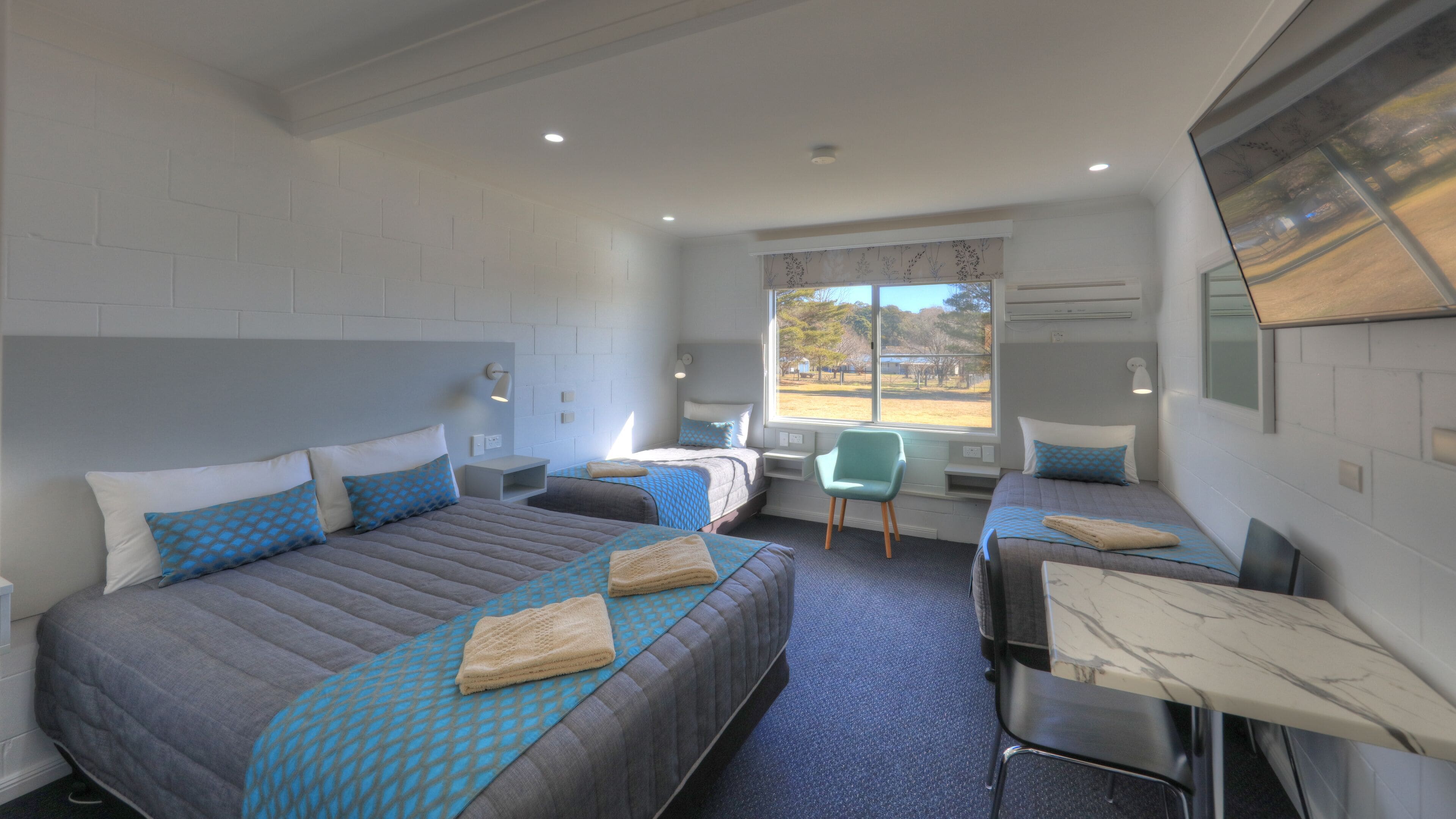 A hotel room with two beds, a desk, and a chair. There is a window with a view of the outdoors.