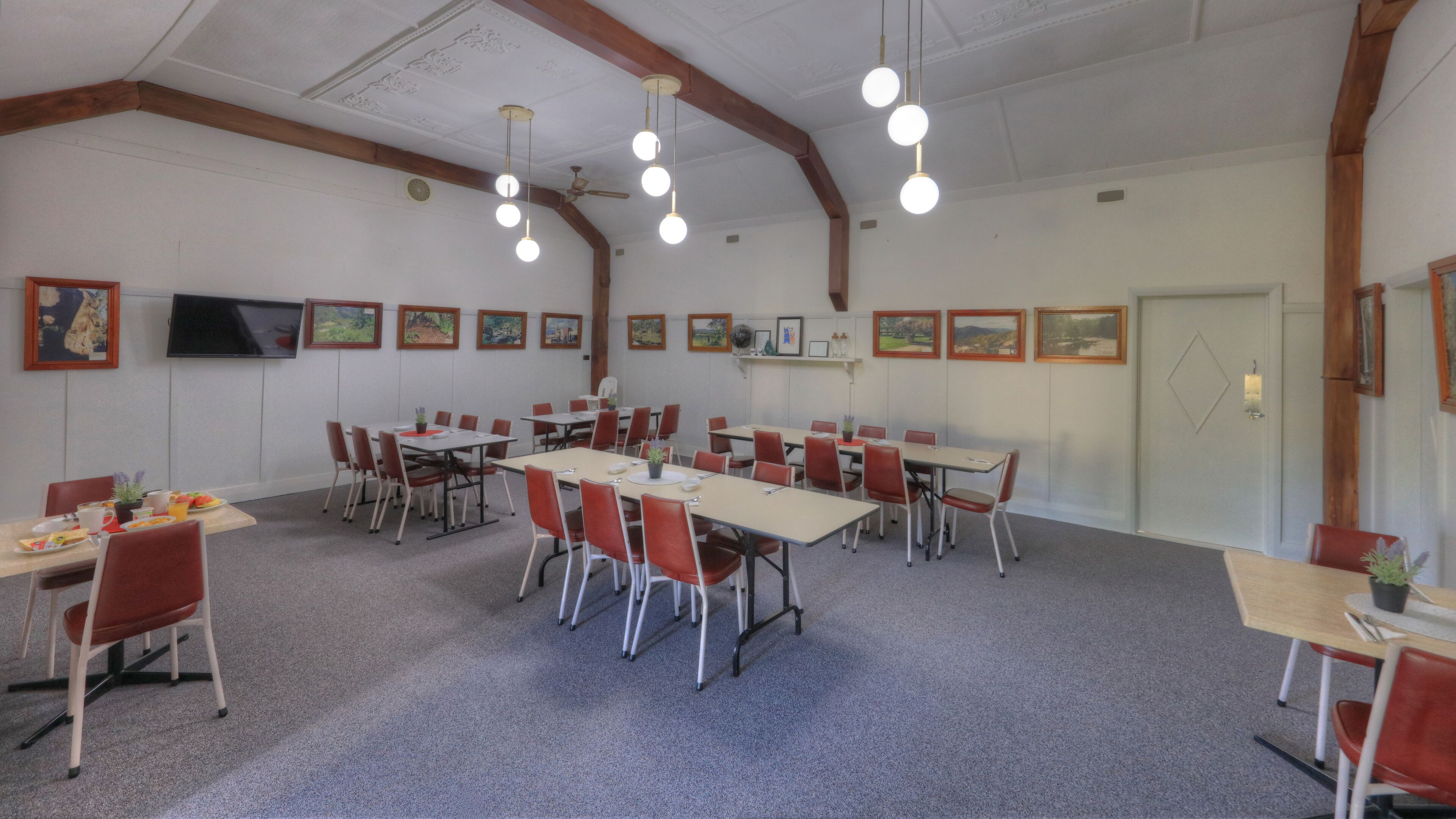 A conference room with multiple tables and chairs, wooden beams on the ceiling, and framed pictures on the walls.