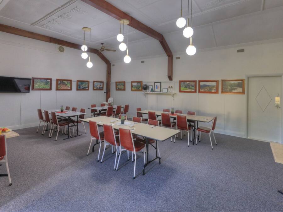 A conference room with multiple tables and chairs, wooden beams on the ceiling, and framed pictures on the walls.