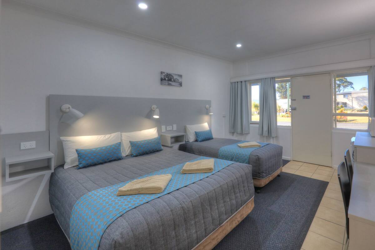 A hotel room with two beds, a desk, a chair, a TV, and a window with curtains.