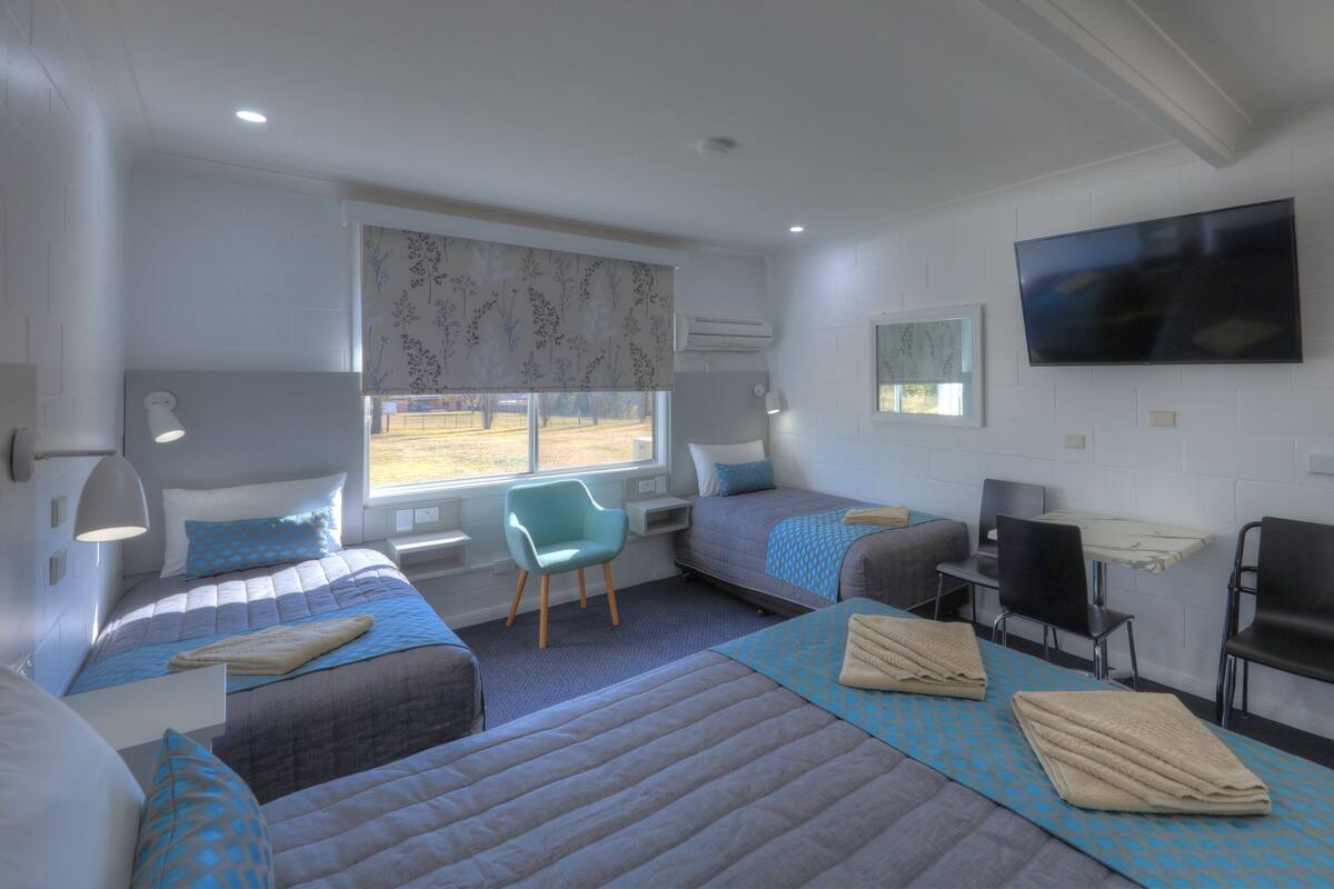 A hotel room with two beds, a desk, a chair, a TV, and a window with a view.