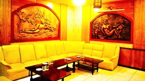 A yellow sofa, a wooden coffee table, and two wall-mounted paintings in a room with a tiled floor. - Asia Hotel Can Tho (Can Tho)