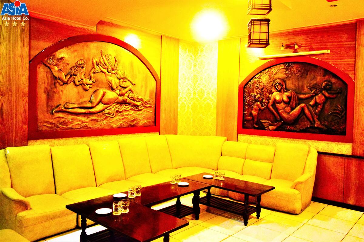 A yellow sofa, a wooden coffee table, and two wall-mounted paintings in a room with a tiled floor.